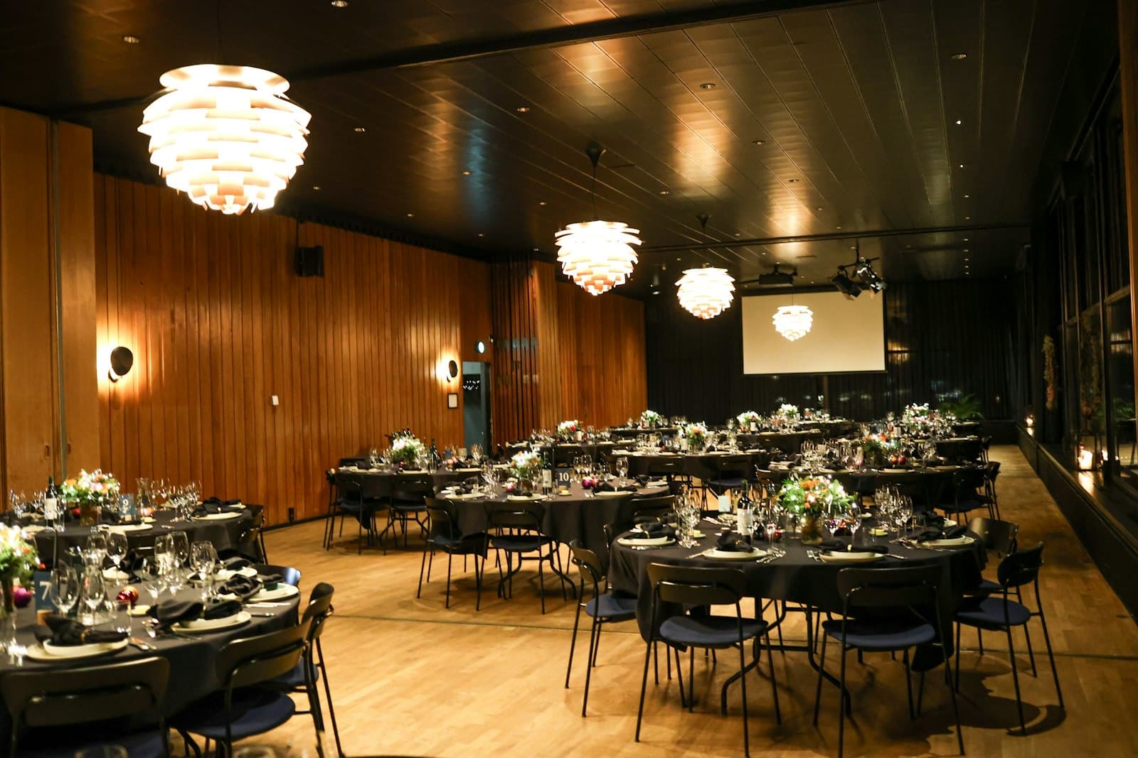 An event hall set with round banquet tables, centrepieces and a projector screen