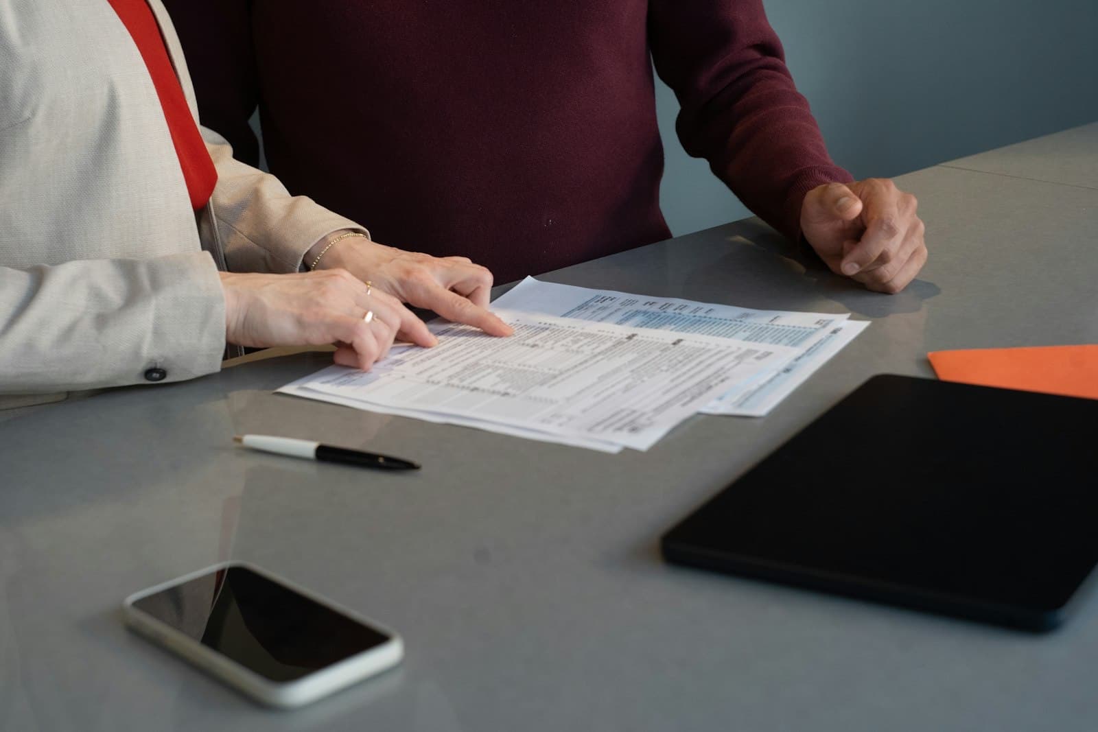 Two people review printed documents together at a grey conference table