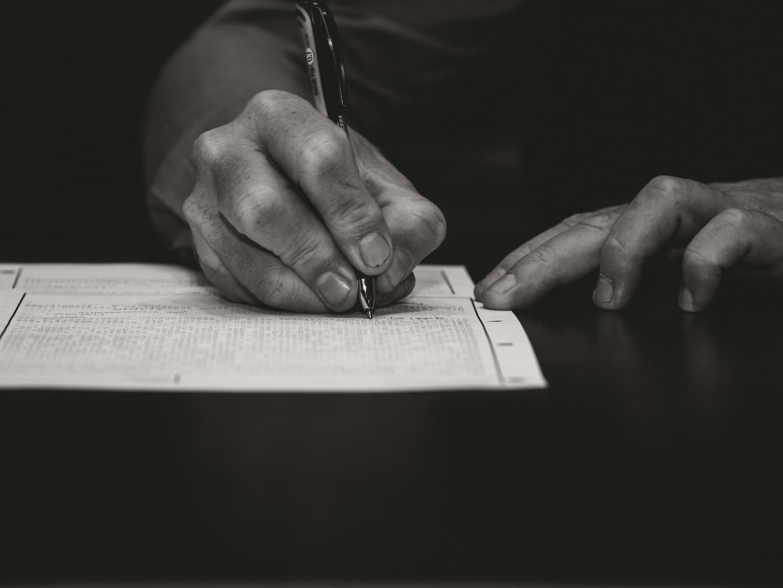 Black-and-white close-up of a hand writing on a form with a fountain pen