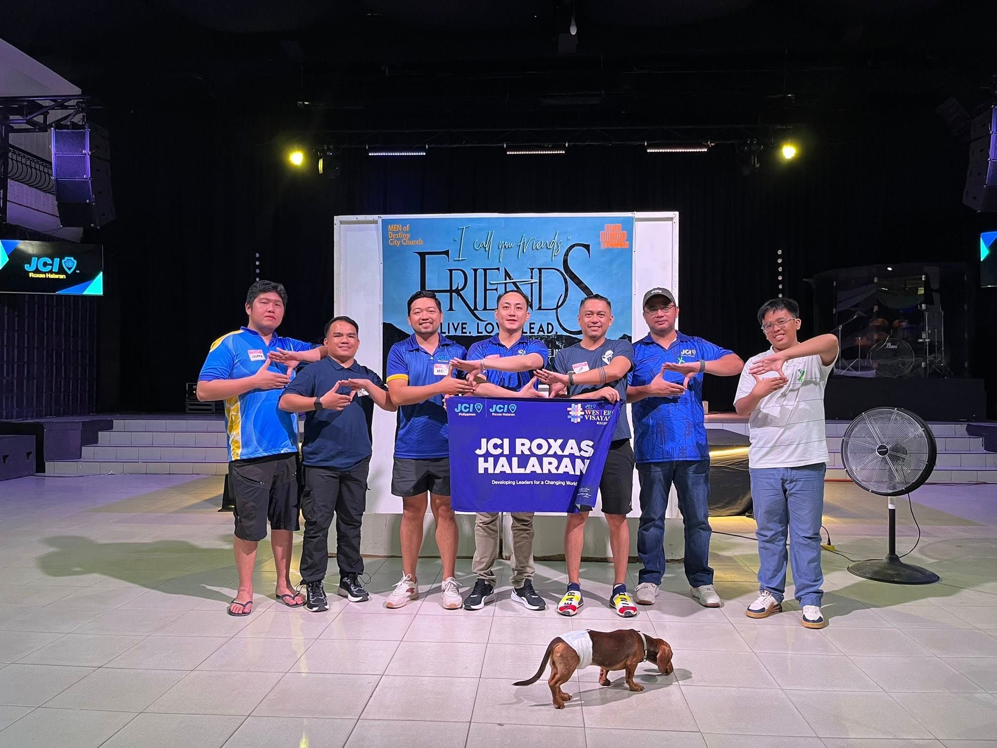 JCI Roxas Halaran members hold the chapter banner on stage at the FRIENDS x JCI Roxas Halaran event